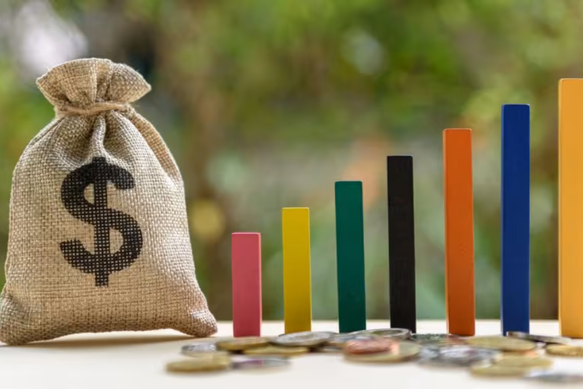 A burlap sack with a dollar sign next to colourful vertical blocks and scattered coins, symbolising budgeting and financial growth.